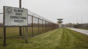 Illinois State Correctional Facility sign beside razor wire fence and guard tower